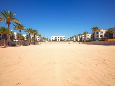 Mixed Use Land in Vendita a Al Rawda, Ajman - A_vast_open_plot_of_land_in_a_suburban_area_showcasing_an_enormous_expanse_of_sandy_ground_bordered_by_a_low_wall. _The_scene_is_bright_and_sunny_with_palm_trees_scattered_throughout_the_landscape. _In_the_background_m. jpeg