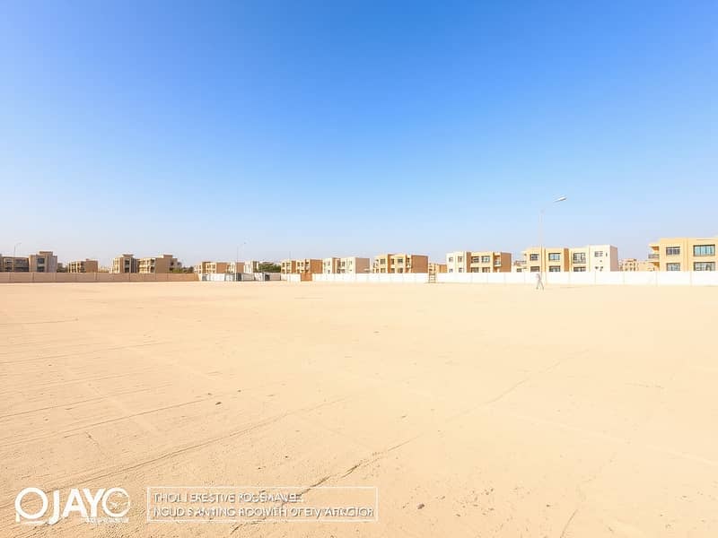 4 A_large_empty_residential_plot_in_the_UAE_situated_one_block_from_a_road. _The_scene_features_an_expansive_flat_sandy_terrain_without_trees_or_signs_creating_an_open_unobstructed_view. _The_sky_is_bright_blue_typic (2). jpeg