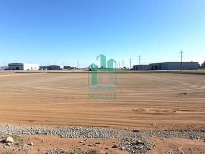 Mixed Use Land te Koop in Al Alia, Ajman - An_empty_industrial_plot_of_land_characterized_by_a_spacious_area_covered_with_dirt_and_gravel_prepared_for_future_construction. _The_surrounding_landscape_shows_several_nearby_industrial_buildings_and_warehouses_with. jpeg