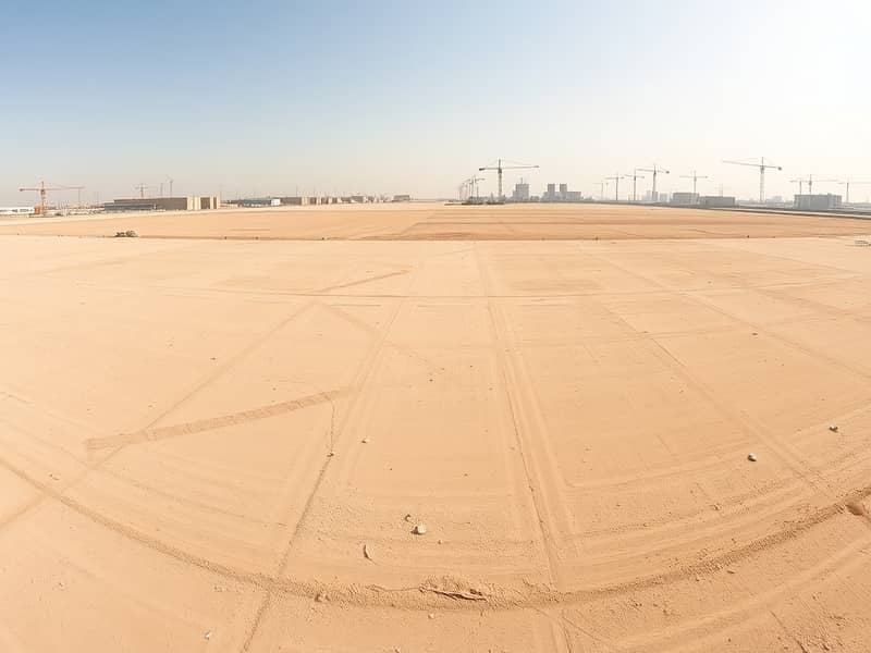 3 A_panoramic_view_of_an_empty_industrial_lot_in_the_UAE_showcasing_a_vast_flat_landscape_marked_for_future_development. _The_ground_is_sandy_and_dry_with_faint_markings_indicating_plot_boundaries. _In_the_distance_there. jpeg