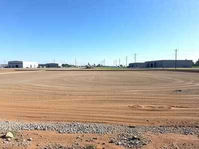 Industrial Land for Sale in Al Sajaa Industrial, Sharjah - An_empty_industrial_plot_of_land_characterized_by_a_spacious_area_covered_with_dirt_and_gravel_prepared_for_future_construction. _The_surrounding_landscape_shows_several_nearby_industrial_buildings_and_warehouses_wit - Copy. jpeg