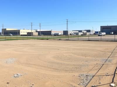 Industrial Land for Sale in Al Sajaa Industrial, Sharjah - An_empty_industrial_plot_of_land_featuring_a_large_flat_area_with_dirt_and_gravel_ready_for_future_development. _The_plot_is_surrounded_by_chain_link_fencing_and_has_a_few_utility_poles_in_the_background. _Nearby_there. jpeg