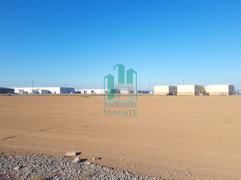 3 A_vast_empty_industrial_plot_of_land_covered_with_dirt_and_gravel_ready_for_future_construction. _In_the_background_there_are_several_nearby_industrial_buildings_and_warehouses_under_a_clear_blue_sky. _Utility_poles_c - Copy. jpeg