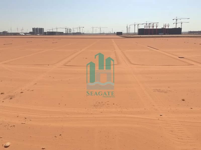 3 A_panoramic_view_of_an_empty_industrial_site_in_the_UAE_featuring_a_vast_leveled_sandy_terrain_marked_with_faint_boundary_lines. _The_ground_appears_dry_and_flat_with_scattered_patches_of_sparse_vegetation. _In_the_bac. jpeg