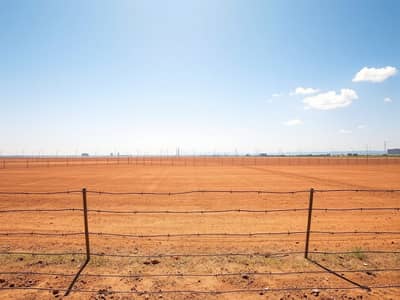 Industrial Land in Vendita a Al Sajaa Industrial, Sharjah - A_wide_view_of_a_barren_industrial_plot_on_a_sunny_day. _The_land_is_flat_and_bare_with_a_dry_reddish_brown_surface. _Surrounding_the_plot_is_a_simple_barbed_wire_fence_that_emphasizes_the_emptiness. _In_the_distance_t - Copy. jpeg