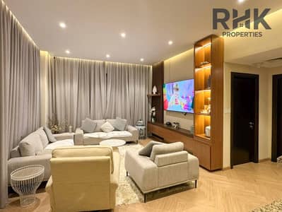 شقة 3 غرف نوم للبيع في مجان، دبي - Furnished living room with sectional sofa, wood TV unit and mounted TV in Dubai apartment