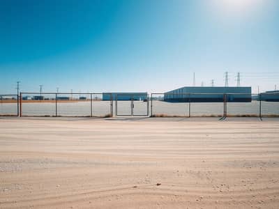 Mixed Use Land for Sale in Al Hamriyah, Sharjah - An_empty_industrial_lot_warehouse_yard_ground_level_wide_angle_photo_style. _Large_flat_gravel_and_dirt_surface_with_subtle_tire_marks_and_scattered_small_stones_beige_dusty_texture. _Perimeter_chain_link_fence - Copy. jpeg