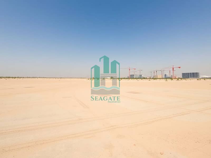3 A_wide_angle_view_of_an_unoccupied_industrial_area_in_the_UAE_under_a_clear_blue_sky. _The_ground_is_a_smooth_sandy_surface_with_subtle_markings_indicating_future_development_plots. _In_the_distance_tall_cranes_and_unf. jpeg
