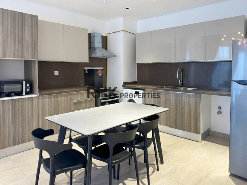 6 Fully fitted kitchen with gas range, washing machine, and marble dining table in furnished JVC apartment