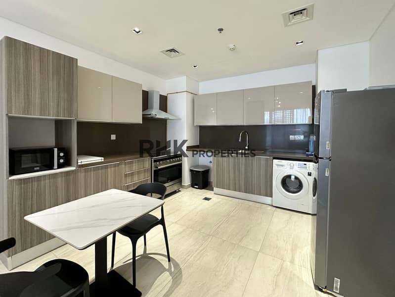 5 Open-plan kitchen with L-shaped fitted cabinets, stainless steel appliances, and dining area in JVC Dubai