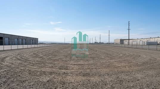 ارض صناعية  للايجار في صناعية الصجعة، الشارقة - A_very_large_empty_industrial_photo_landscape_in_wide_angle_perspective_a_clean_vacant_industrial_yard_with_a_wide_dirt_gravel_ground_distant_warehouse_buildings_on_the_left_and_right_a_tall_chain_link_fence_enclosing. png