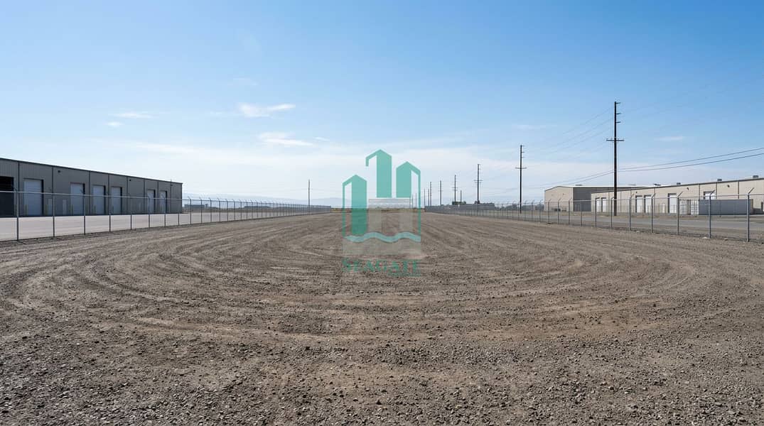 A_very_large_empty_industrial_photo_landscape_in_wide_angle_perspective_a_clean_vacant_industrial_yard_with_a_wide_dirt_gravel_ground_distant_warehouse_buildings_on_the_left_and_right_a_tall_chain_link_fence_enclosing. png A_very_large_empty_industrial_photo_landscape_in_wide_angle_perspective_a_clean_vacant_industrial_yard_with_a_wide_dirt_gravel_ground_distant_warehouse_buildings_on_the_left_and_right_a_tall_chain_link_fence_enclosing. png
