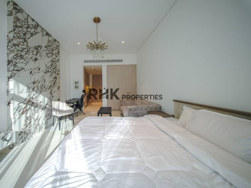 3 Furnished studio apartment with king bed, marble accent wall, chandelier and integrated workspace in Dubai