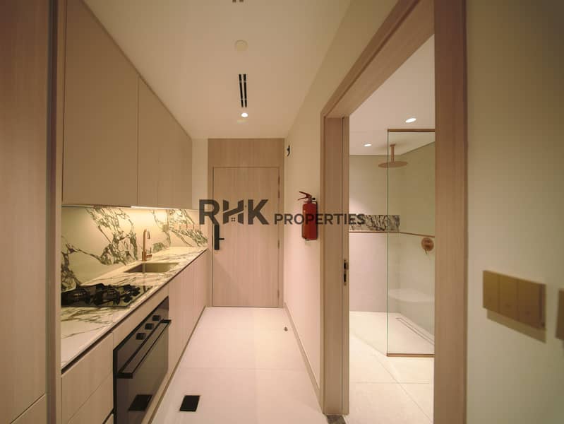 6 Galley kitchen and glass walk-in shower in warmly lit furnished Dubai studio apartment Primary keyword: furnished Dubai studio apartment