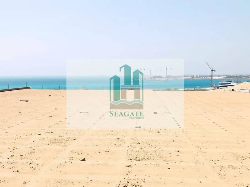 2 A_large_flat_empty_plot_of_land_with_a_clear_view_of_the_sea_in_Ajman_resembling_a_construction_site. _The_terrain_is_mostly_barren_with_light_beige_sand_and_some_tire_tracks_visible_across_the_surface. _In_the_backgro. jpeg