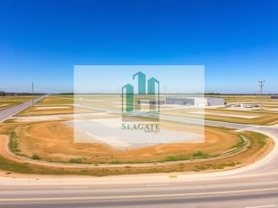 Industrial Land te Koop in Al Jurf, Ajman - A_broad_view_of_industrial_land_containing_several_empty_lots_available_for_development. _The_area_showcases_flat_terrain_with_a_mixture_of_gravel_and_grass_surrounded_by_access_roads. _A_few_industrial_buildings_are_i. jpeg