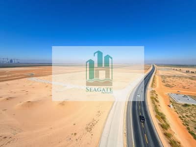 Земля промышленного назначения Продажа в Аль Джурф, Аджман - An_expansive_view_of_a_barren_landscape_resembling_a_construction_site_with_clear_blue_skies_above. _The_ground_is_primarily_sandy_with_some_patches_of_sparse_vegetation. _On_one_side_a_wide_road_runs_through_the_lands. jpeg