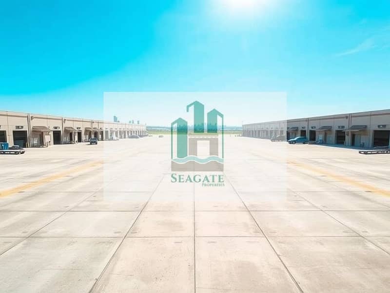2 A_vast_industrial_plot_featuring_a_large_concrete_surface_that_extends_into_the_distance_bordered_by_multiple_rows_of_substantial_warehouse_buildings. _The_scene_is_under_a_clear_blue_sky_with_bright_sunlight_creating. jpeg