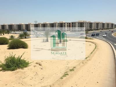 Mixed Use Land te Koop in Al Alia, Ajman - A_plot_of_land_situated_next_to_a_building_community_along_a_main_road_in_the_UAE. _The_scene_shows_a_sandy_terrain_with_some_foliage_and_a_few_palm_trees. _In_the_background_modern_residential_buildings_are_lined_ (2). jpeg
