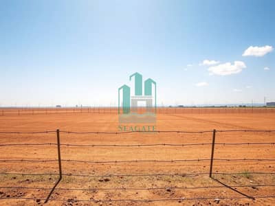 Industrial Land zum zum Verkauf in Al Hayl, Fujairah - A_wide_view_of_a_barren_industrial_plot_on_a_sunny_day. _The_land_is_flat_and_bare_with_a_dry_reddish_brown_surface. _Surrounding_the_plot_is_a_simple_barbed_wire_fence_that_emphasizes_the_emptiness. _In_the_distance_th. jpeg