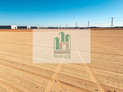 Industrial Land for Rent in Al Sajaa, Sharjah - A_large_empty_industrial_land_plot_similar_to_the_reference_image_wide_open_dusty_gravel_lot_with_light_brown_dirt_subtle_tire_tracks_graded_soil_texture_scattered_small_rocks_no_buildings_in_the_foreground_distant_i. jpeg