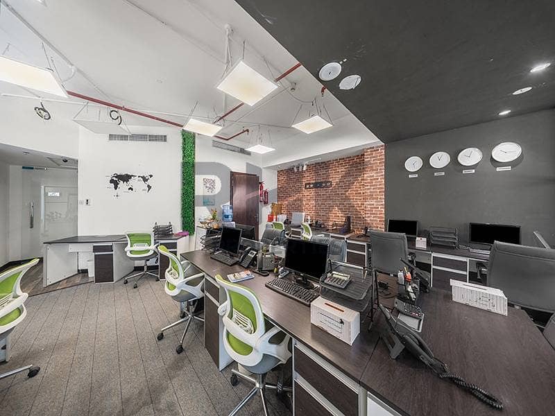 21 Open-plan office with world clocks, brick wall and green workstations in JLT Dubai