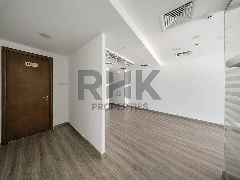 6 Fitted office in Ontario Tower Business Bay showing washroom entrance, open work area and laminate flooring under a recessed ceiling