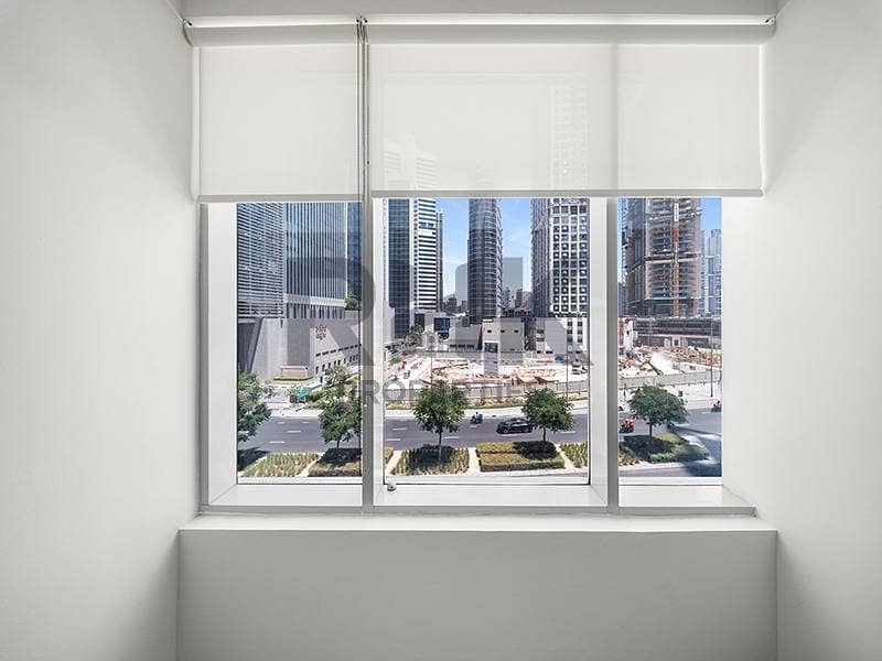 21 Office window view in Ontario Tower Business Bay overlooking high-rise towers and a landscaped street, with roller blinds and white sill