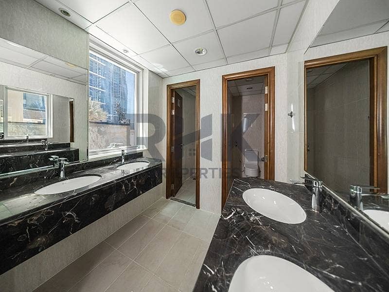 25 Shared office washroom in Ontario Tower Business Bay with marble vanity, dual sinks, mirrors and a tower view window, fitted and ready