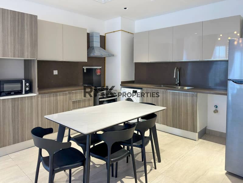 6 Fully fitted kitchen with gas range, washing machine, and marble dining table in furnished JVC apartment