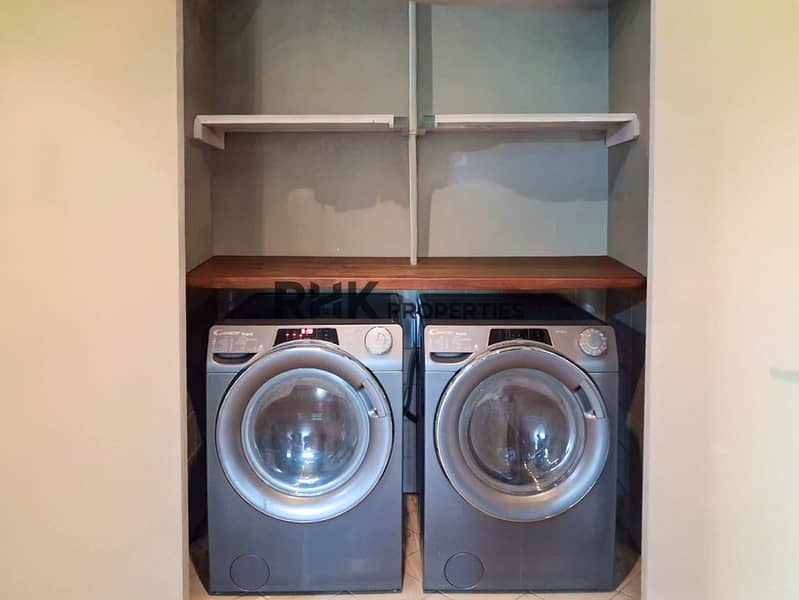 12 ilt-in laundry alcove with dual Candy washing machines and wooden countertop