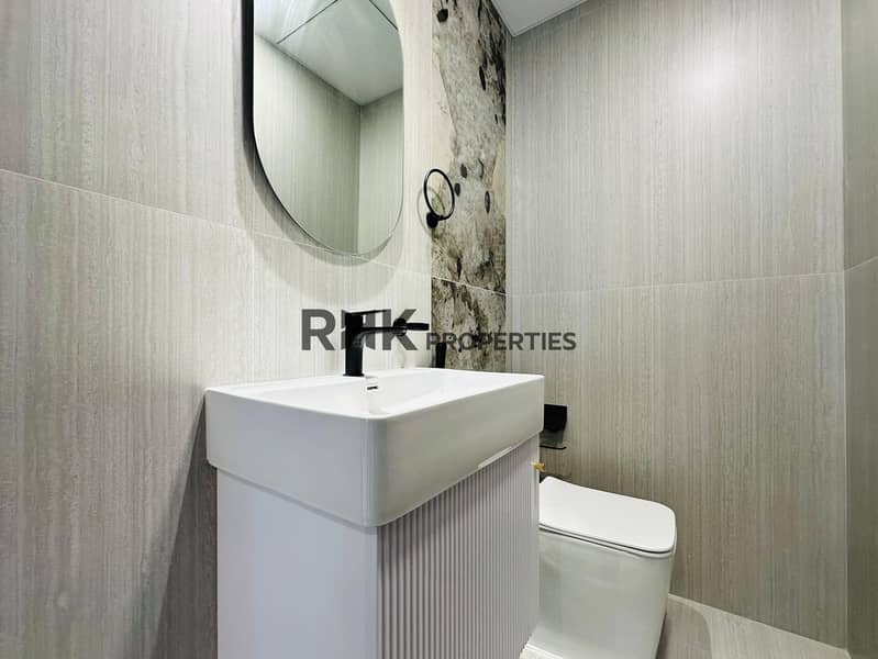 9 Modern bathroom with grey travertine tiles, white wall-mounted basin, matte black faucet, round frameless mirror, and accent marble feature wall in Dubai apartment