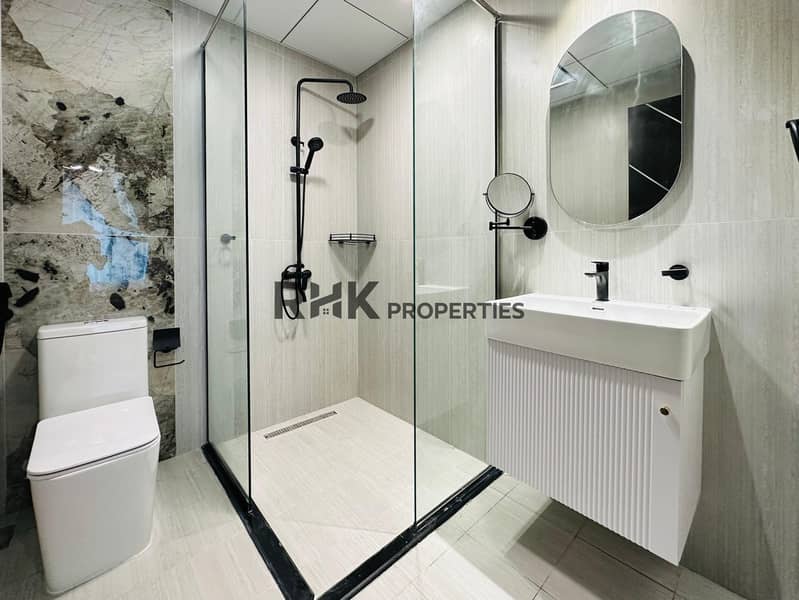 10 Luxury en-suite bathroom with glass shower enclosure, matte black rain shower, wall-mounted basin, travertine tiles, and dramatic marble feature wall in Dubai apartment