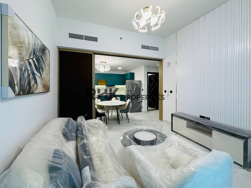 3 Brand new furnished apartment living room with ribbed accent wall, TV unit, sofa set, designer chandelier, and open-plan kitchen visible through gold-framed sliding partition in Dubai