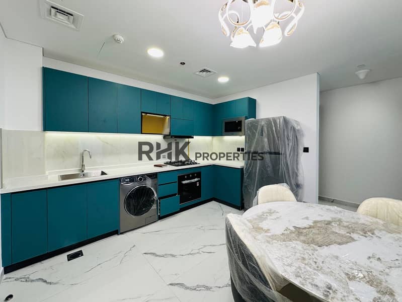 5 Bright furnished kitchen and dining area with teal flat-panel cabinets, marble round dining table, stainless steel appliances, washing machine, and gold chandelier in Dubai