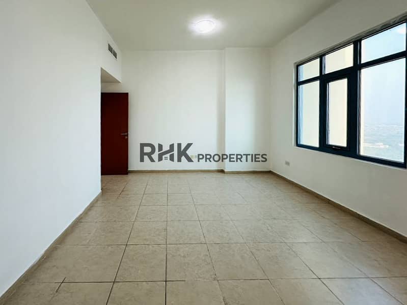 3 Bright unfurnished bedroom with floor-to-ceiling city view windows, beige tile flooring, and built-in AC vent in Dubai high-rise apartment