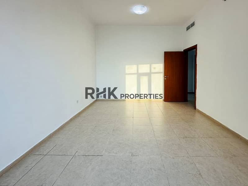 7 Bright unfurnished bedroom with warm sunlight, wooden door, tiled floor, and central AC vent in Dubai residential apartment
