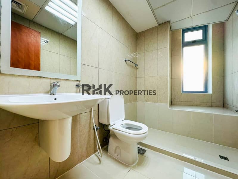 11 Modern bathroom with bathtub, pedestal sink, toilet, beige marble wall tiles, and natural light window in Dubai apartment