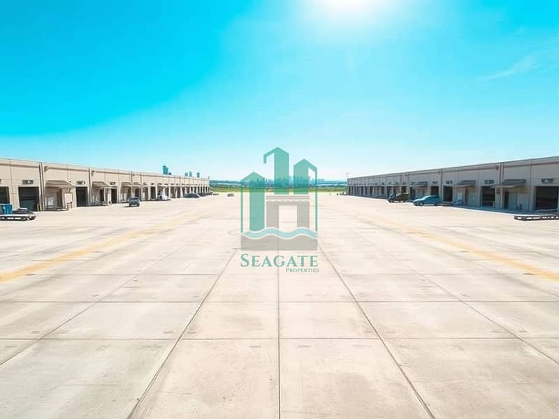 2 A_vast_industrial_plot_featuring_a_large_concrete_surface_that_extends_into_the_distance_bordered_by_multiple_rows_of_substantial_warehouse_buildings. _The_scene_is_under_a_clear_blue_sky_with_bright_sunlight_creating. jpeg