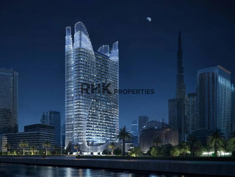 15 Luxury Dubai residential tower fully illuminated at night with Burj Khalifa visible in skyline, organic wavy glass facade glowing under moonlit sky