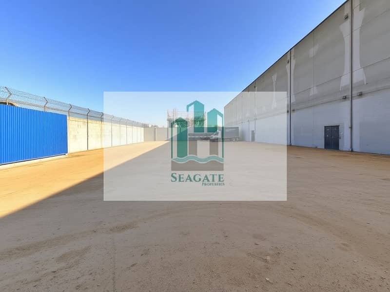 2 A_spacious_industrial_yard_similar_to_the_one_shown_with_a_large_empty_area_of_bare_ground_that_has_been_slightly_expanded. _Surrounding_the_yard_there_are_tall_sturdy_concrete_walls_for_security_with_a_blue_corrugate. jpeg