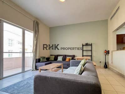 شقة 1 غرفة نوم للايجار في قرية جميرا الدائرية، دبي - Spacious apartment living room with sectional sofa, TV, coffee table and balcony access