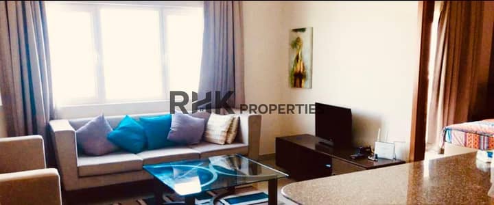 1 Bedroom Apartment for Sale in Downtown Jebel Ali, Dubai - Living room with a beige sofa, blue and grey cushions, a glass coffee table and a window with curtains.