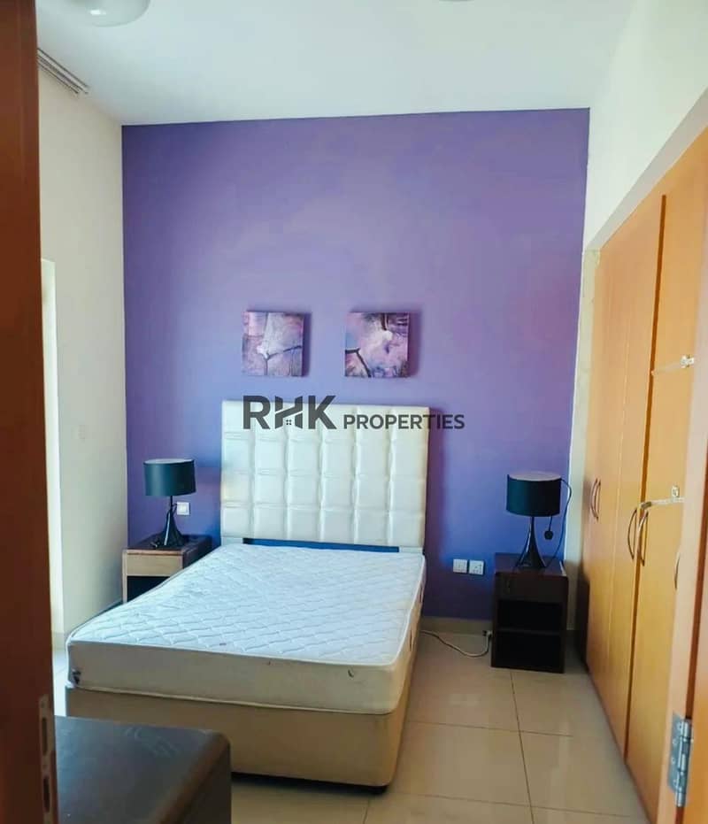 2 Bedroom with a white bed, a purple accent wall, two bedside tables with black lamps and a wooden wardrobe.