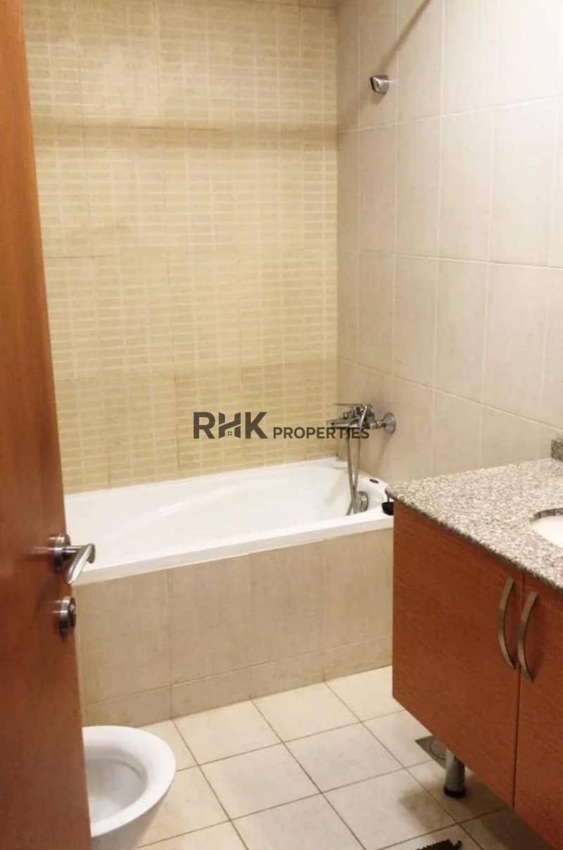 6 Bathroom showing the bathtub with a wall-mounted shower, beige tiles and a wood-effect vanity.