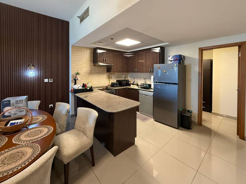 4 Open kitchen and dining area with dark cabinets, stainless fridge and oval dining table.