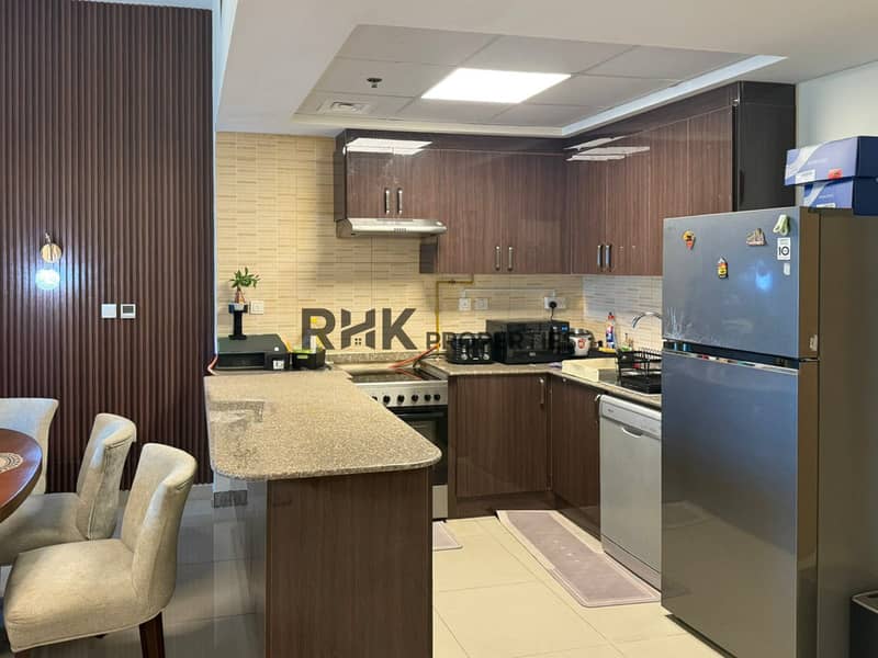 5 Closed kitchen with dark wood cabinets, breakfast counter, stainless fridge and dining chairs.