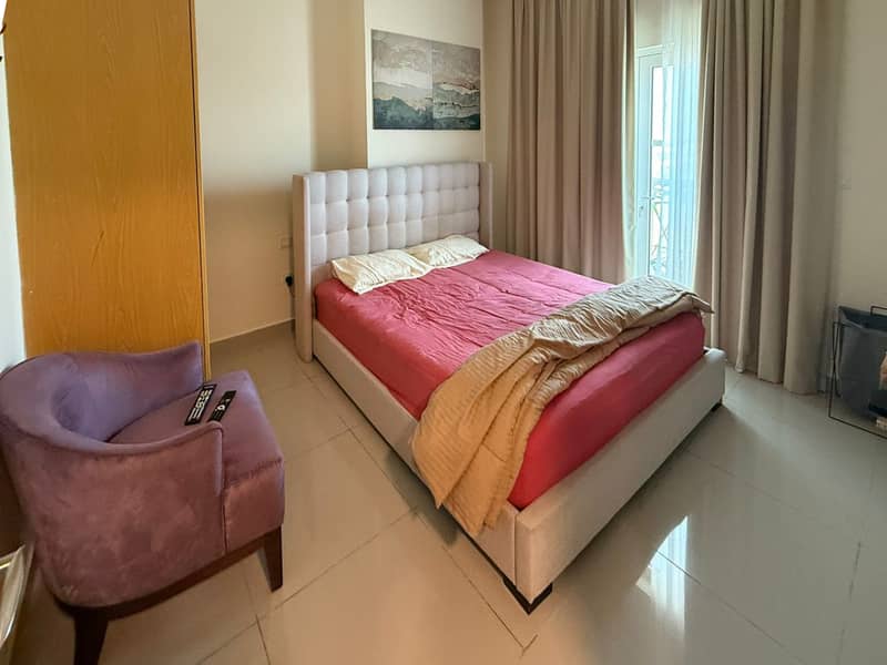 7 Bedroom with pink bedding, purple armchair and grey curtains drawn over the window.