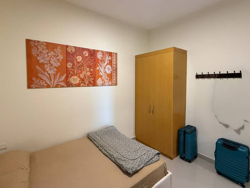 9 Bedroom with single bed, wooden wardrobe, floral wall art and two blue suitcases on the floor.