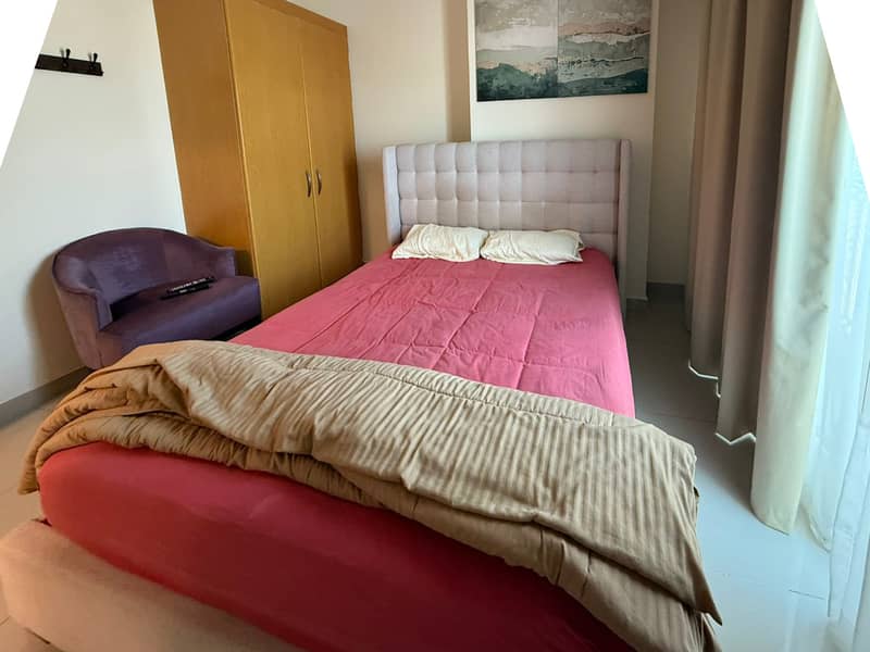 11 Bedroom with pink bedding, tall wooden wardrobe and purple armchair.